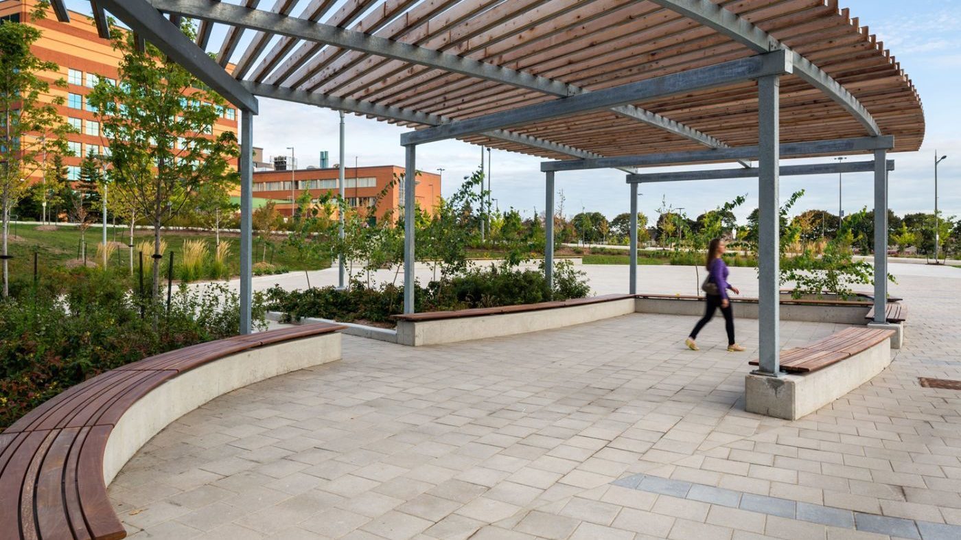 Woman walks under an arbor with wall mounted wood benches surrounding