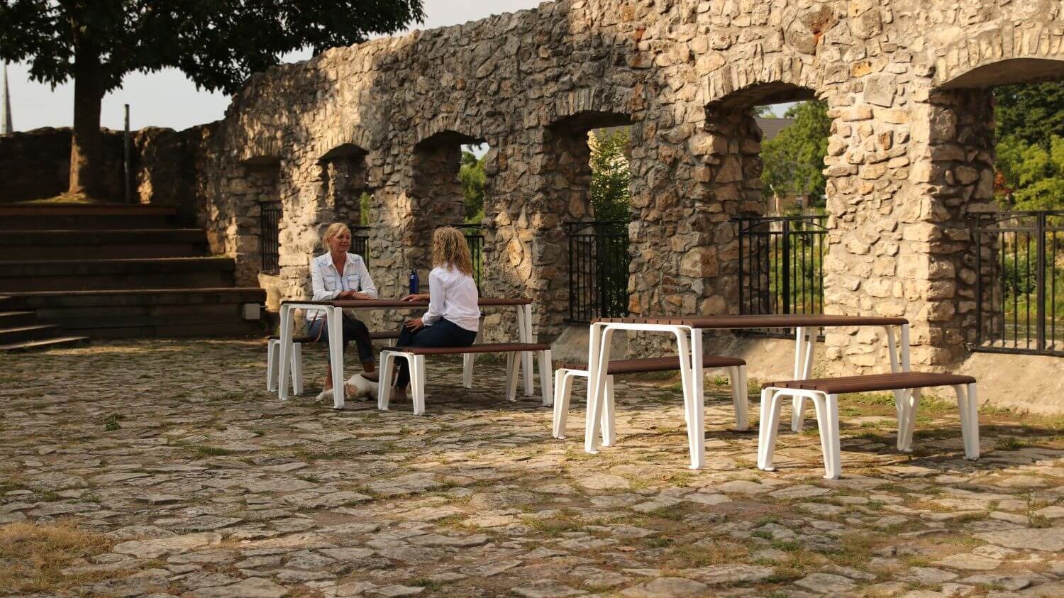 white legged tables with wood top. In the background two women are sitting at a table