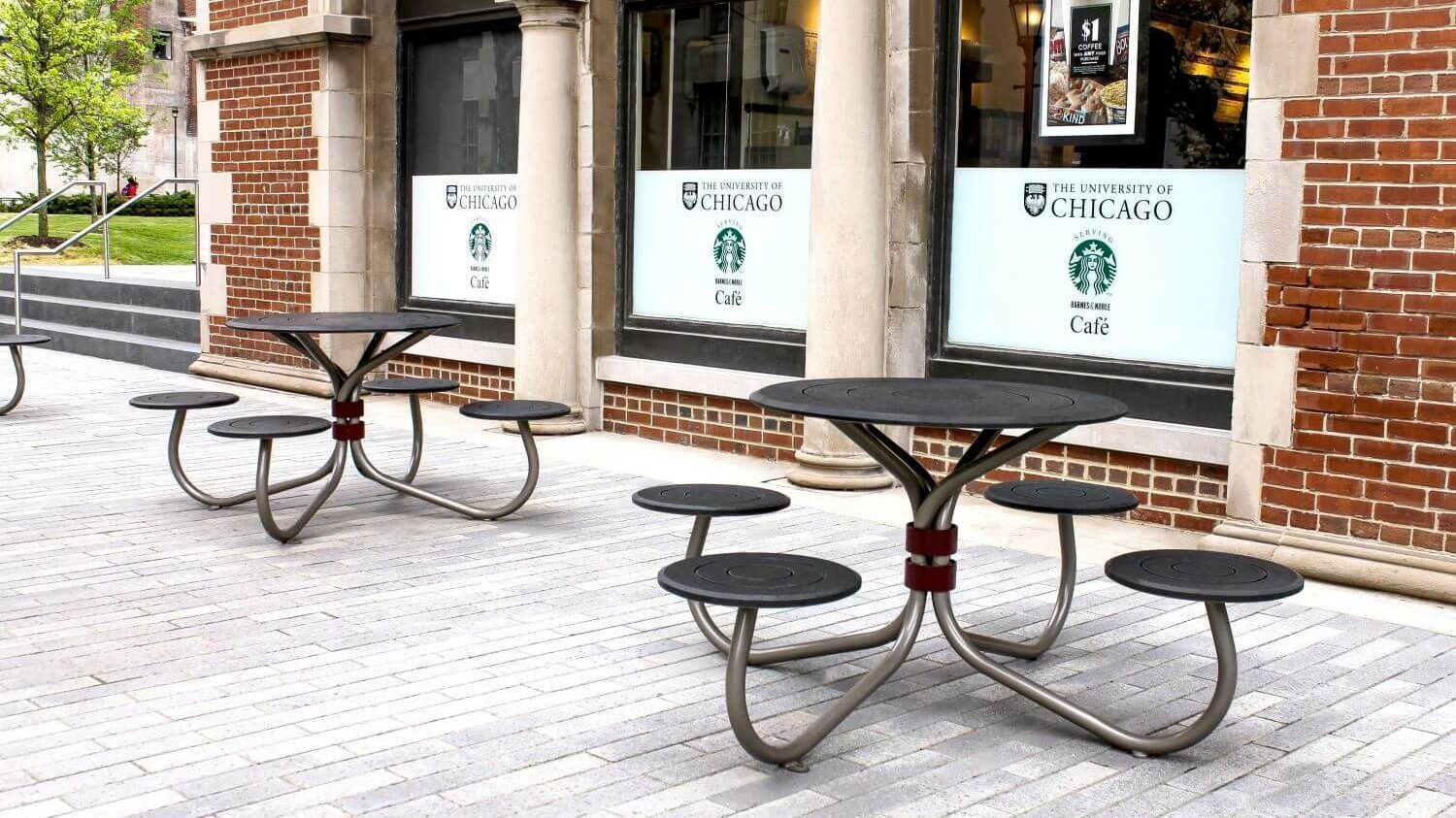 Black tables with four round seats outside red brick building