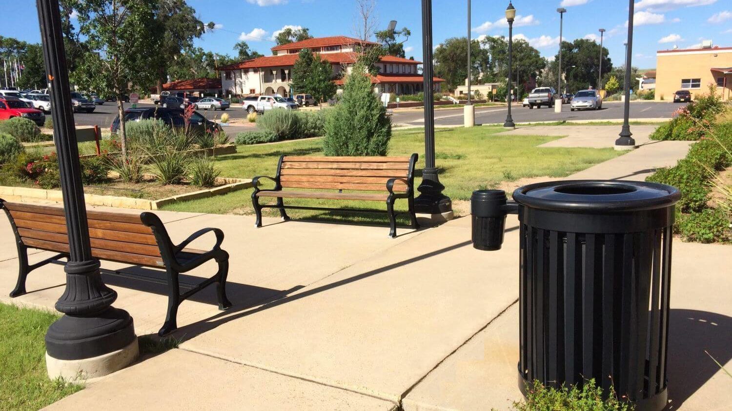 Black trash can near wooden benches and walking paths.