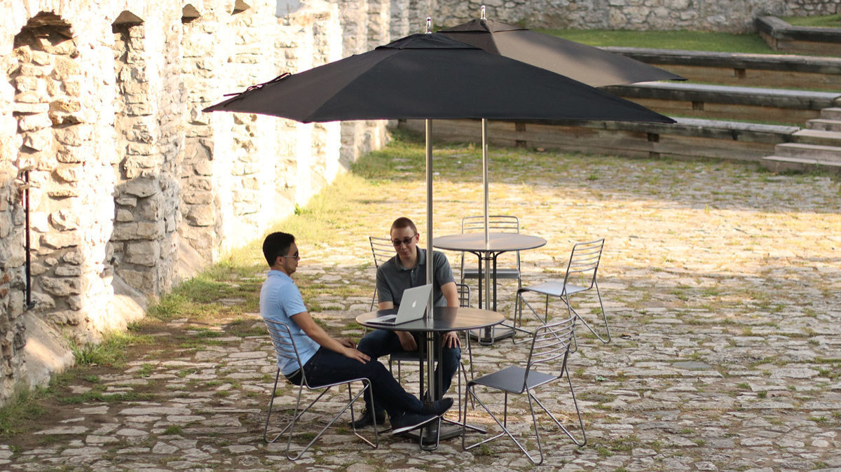 Two men sitting at Kontur table with umbrella