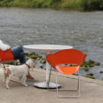 Woman and Dog sitting on Orange Battery Collection Chairs facing the river