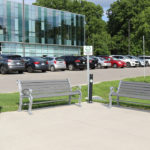 Black trash container with two grey benches and ash receptacle in front of Fit4Less