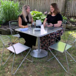 Two women sitting at metal Patio table in a backyard setting