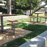 Three wooden tables with individual seatings outside on greens area