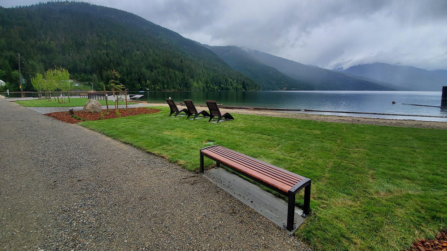 Three lounge chairs and a wood bench overlook a calm lake