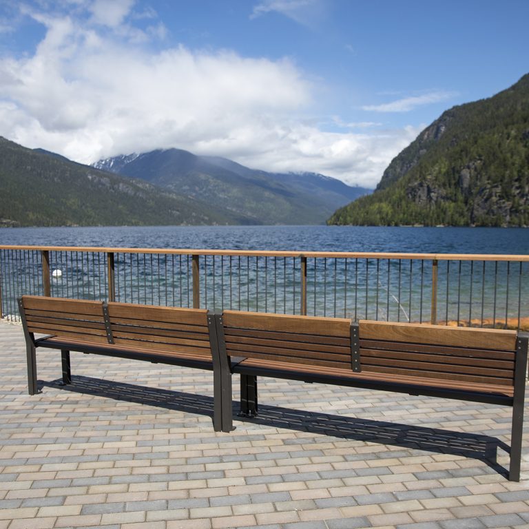 Two wood benches on a paved breakwater overlooking a lake and mountains