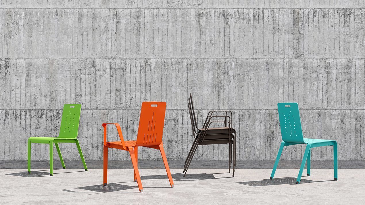 From left to right, light green alum dining chair, orange alum dining chair with arms, stack of 3 bronze Alum dining chairs with arms, and turquoise Alum dining chair lined up in front of a concrete wall.