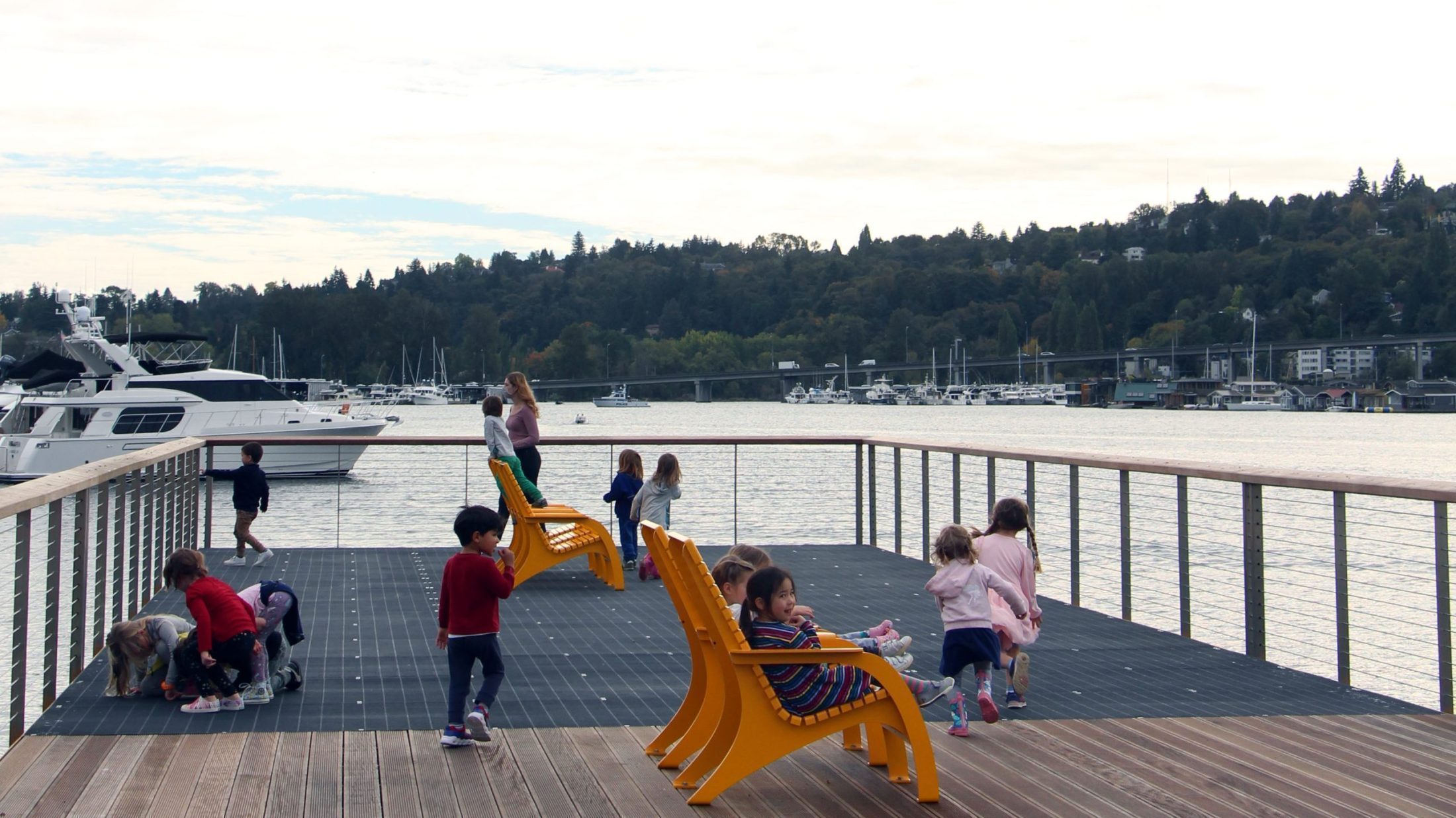 Children sit on yellow lounge chairs on a pier overlooking a waterway