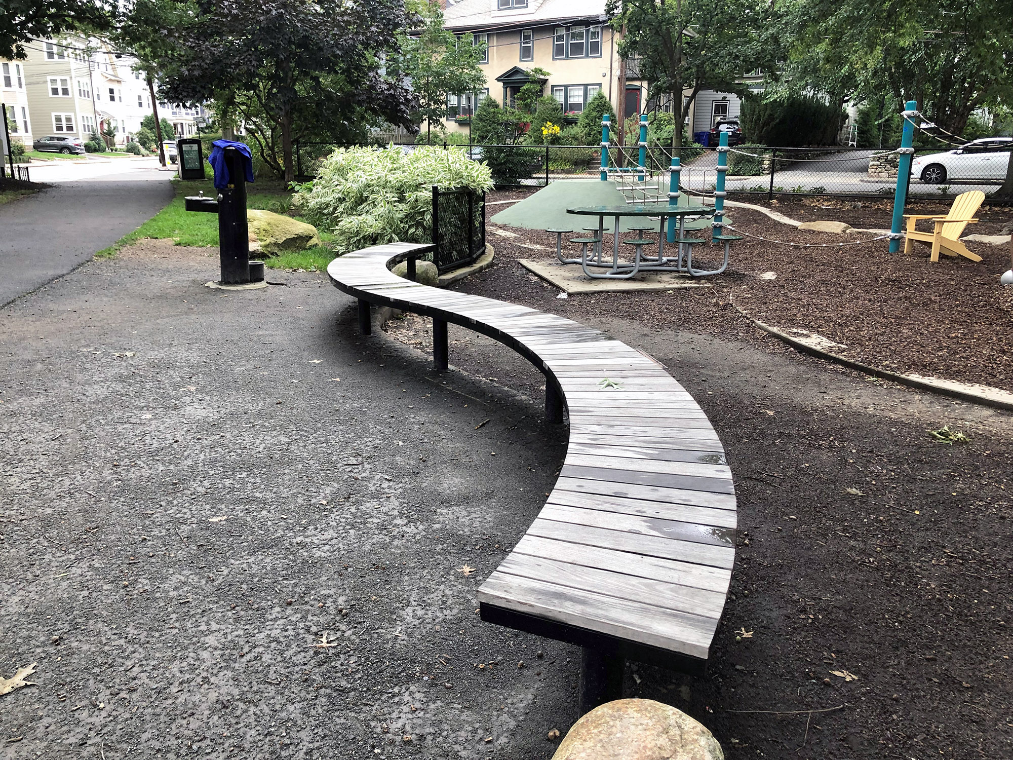 A curved wooden Ogden bench is to the left of a small playground.