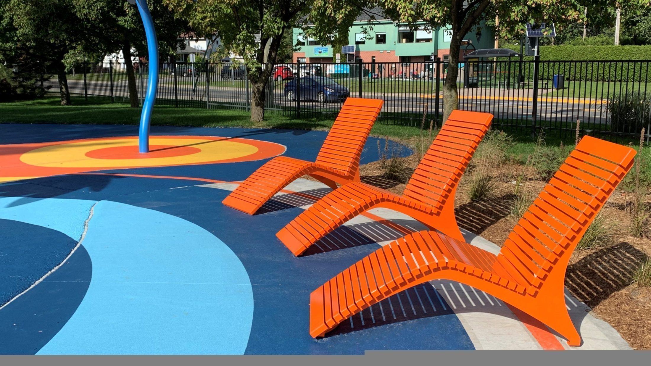 Three Orange 720 Lounge Chairs face a splash pad in a park.