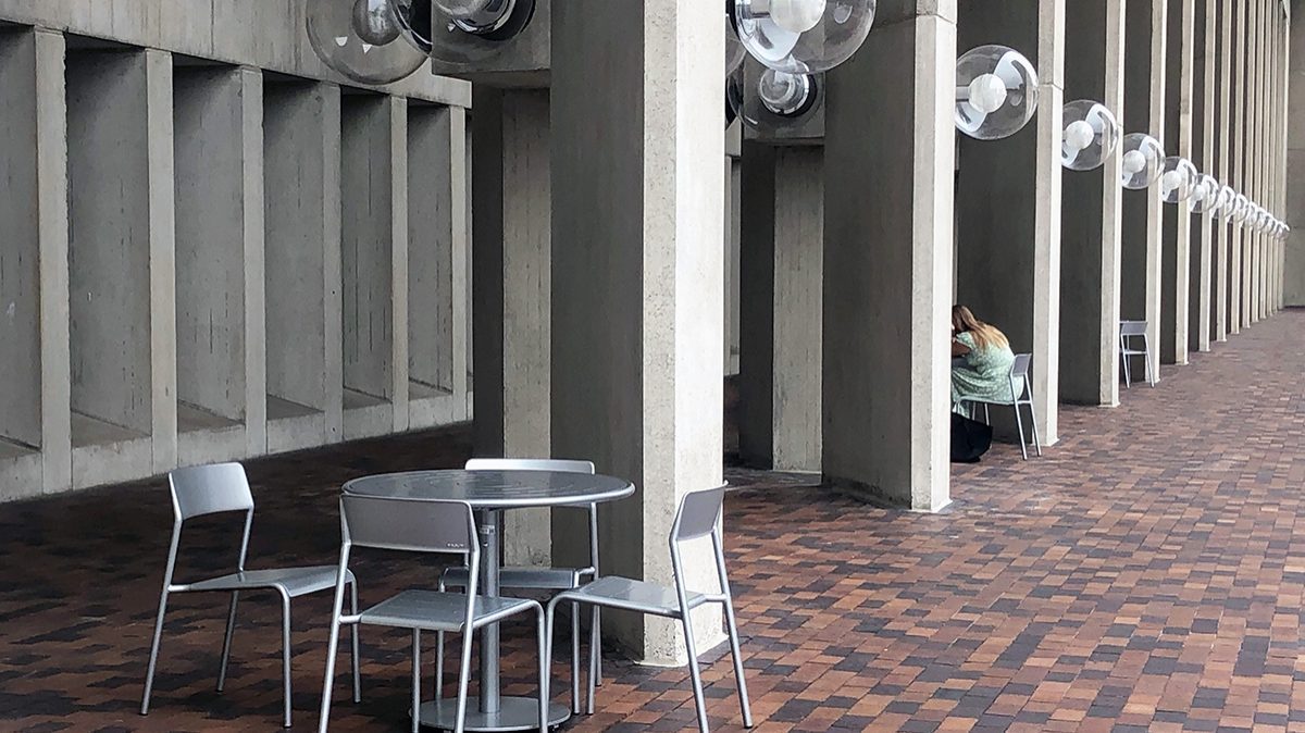 Three sets of Foro tables and chairs are show next to a concrete building.