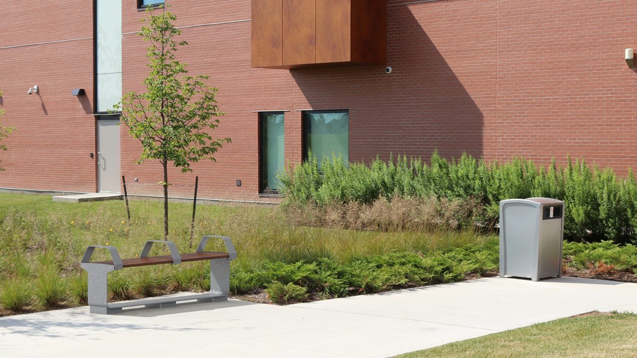 L-Series backless bench next to greenery and building