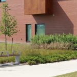 L-Series backless bench next to greenery and building