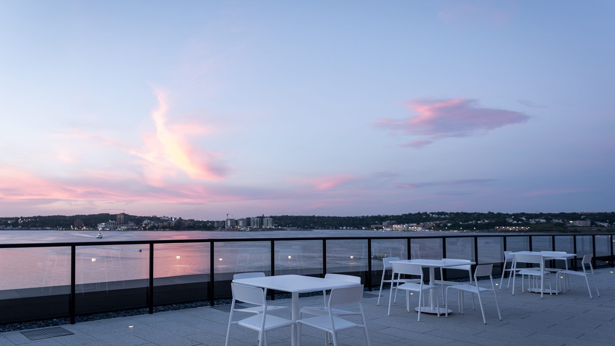 Evening view of white Foro tables and chairs overlooking the ocean from the Stewart McKelvey rooftop terrace