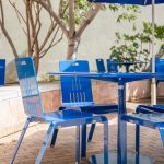 ALUM Chairs painted bright blue with a Foro table on a patio with trees in the background