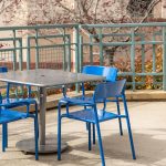 Square Foro Table and Seating, blue and gunmetal powdercoat on a patio with fence in background