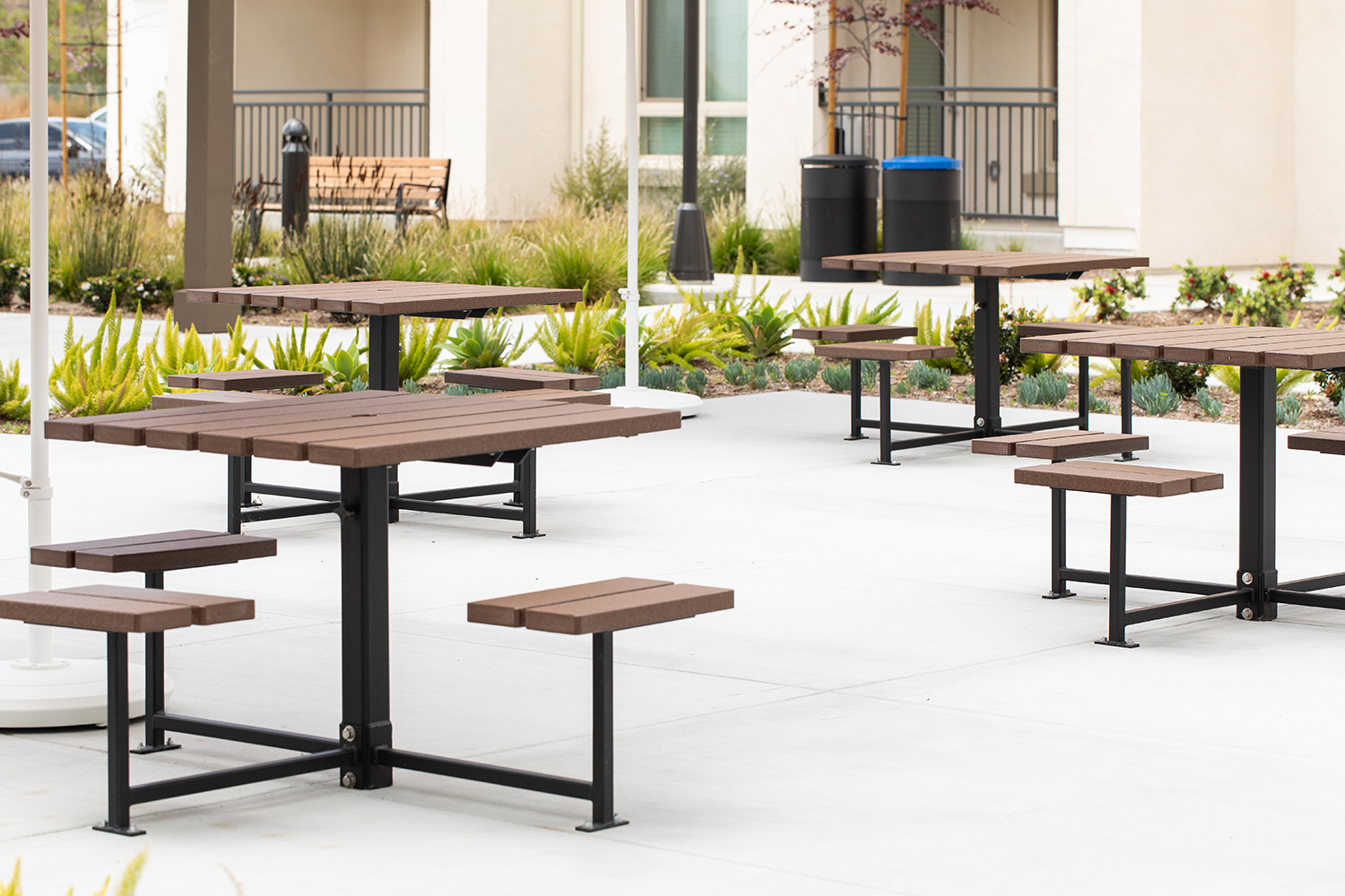 Maglin 400 Series cluster seating units are installed in an amenity courtyard at an apartment complex in Chula Vista, CA. A maglin Iconic Collection bench and waste and recycling containers are in the background as well as a bed of green plants.