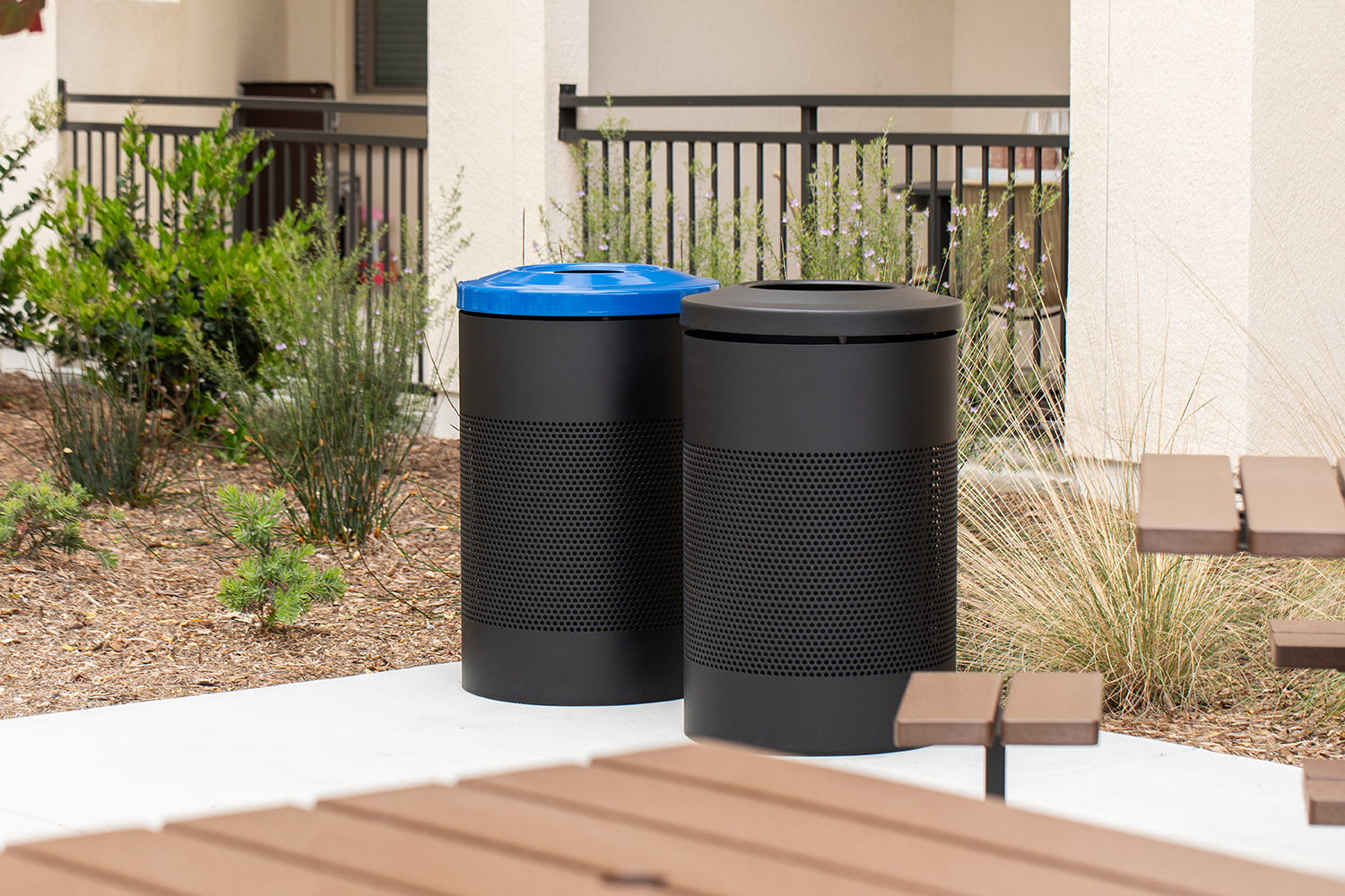 Maglin 600 Series black Recycling and Waste containers are placed in the amenity courtyard of an apartment in Chula Vista, CA. The recycling container has a blue lid to denote its purpose.