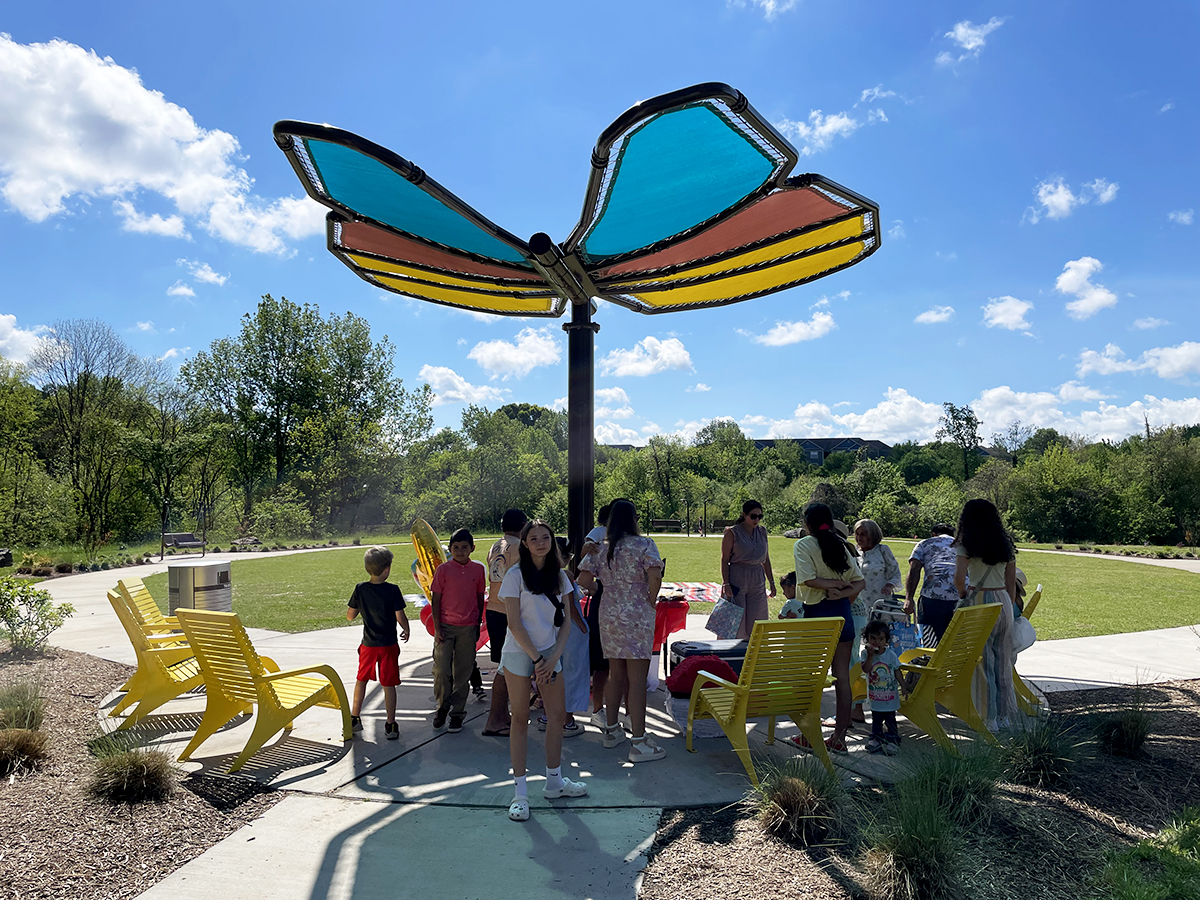 A family celebrates a birthday underneath a butterfly-shaped shade structure at Rosedale Nature Park in Huntersville, NC. Some family members sit in Maglin yellow 720 Chairs.