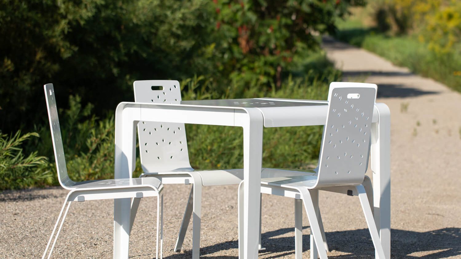 Powdercoated white ALUM table with seating on outdoor patio surrounded by greenery